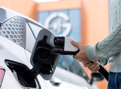 A person plugging an EV charger into a car, representing the fast-charging infrastructure used by both current and future solid-state battery vehicles.