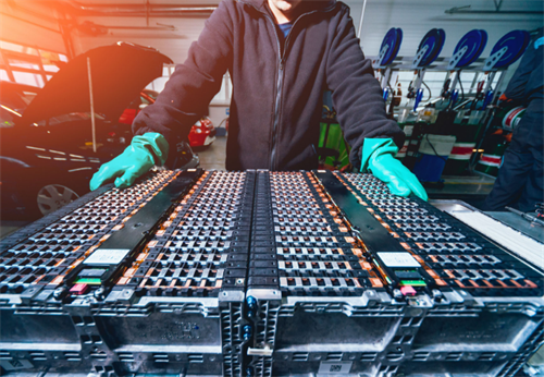 A technician working on a large, heavy traditional lithium-ion EV battery pack, contrasting with the lighter potential of solid-state designs.
