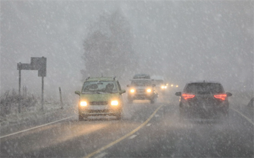 Vehicles driving on a snow-covered highway during a heavy snowstorm, testing driver assistance systems in low-visibility conditions.
