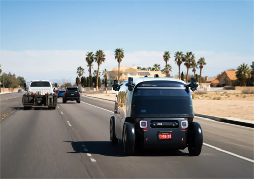 A Zoox robotaxi driving on a public road, representing the consumer-facing autonomous ride-hailing service.